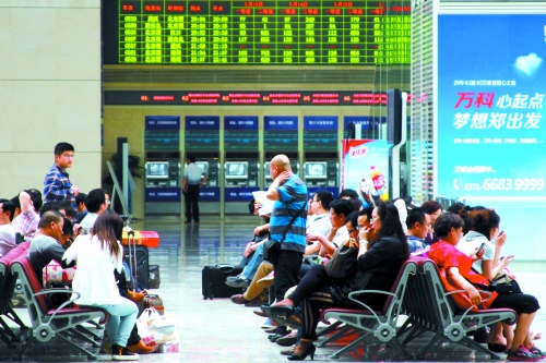 候車大廳溫度很高，一名乘客一手扇風(fēng)、一手擦汗