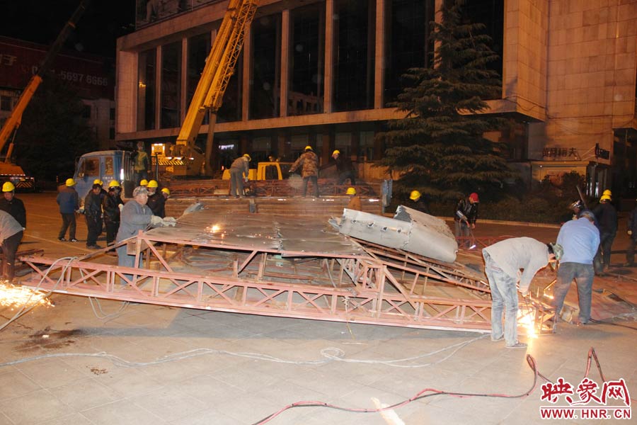 地面上的20多名工人對吊裝下的廣告牌進行分割。