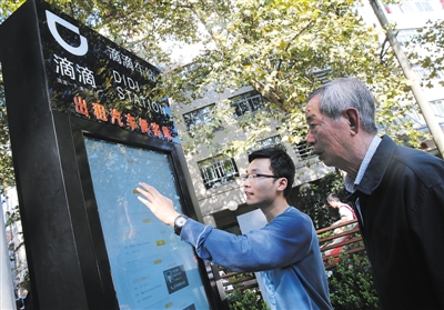 10月15日，滴滴工作人員（左）指導(dǎo)乘客使用“滴滴車站”的電子屏預(yù)約出租車。