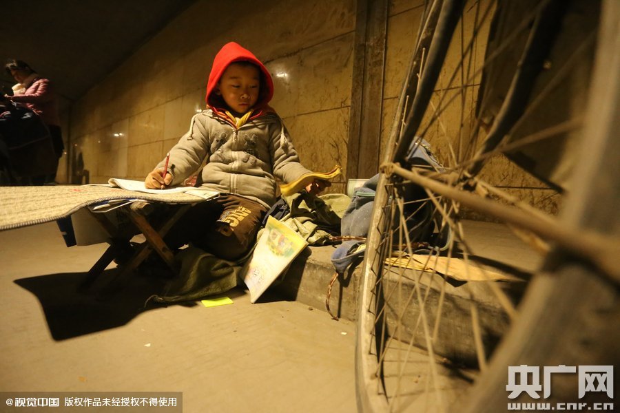 2015年11月8日晚，鄭州，7歲男孩涵洞橋下陪父母練攤，路邊燈下坐小馬扎上寫作業(yè)。