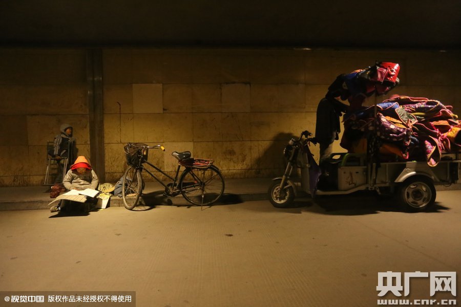 2015年11月8日晚，鄭州，7歲男孩涵洞橋下陪父母練攤，路邊燈下坐小馬扎上寫作業(yè)。