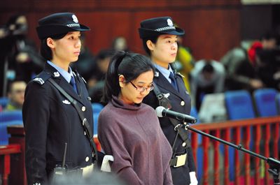 被告人盧梅低著頭，站在朝陽法院刑事審判庭的被告席上。